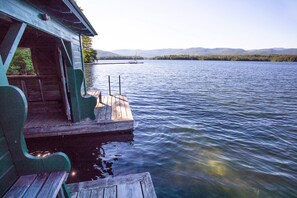 A wooden dock extending into a calm lake with a cabin on the left and a distant shoreline with trees and hills. - Family Retreat on Squam Lake, Tennis, Kayaks, Paddleboards, Dock. (Moultonborough)