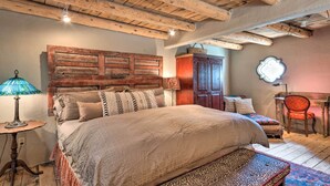 A bedroom with a wooden headboard, a bed with patterned bedding, a small table with a lamp, a chair, and a desk with a lamp. - Chic Adobe-Style Bungalow in Historic Santa Fe! (Santa Fe)