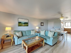 A living room with a light blue sofa set, a glass-top coffee table, and a dining area with a white table and chairs.