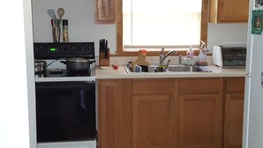 A kitchen with a stove, oven, sink, and wooden cabinets. - Cozy Cottage close to the Lake (Harbert)