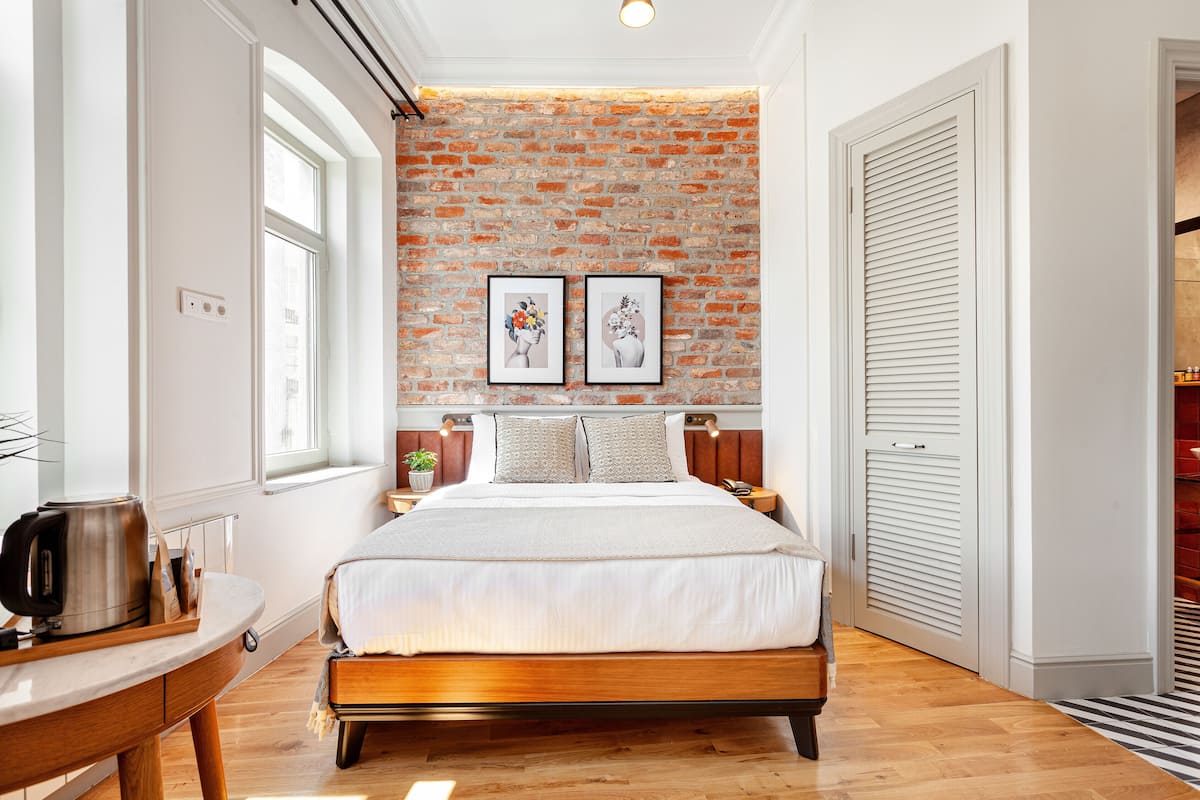 A bedroom with a brick wall, a bed, a nightstand, a window, and a door.