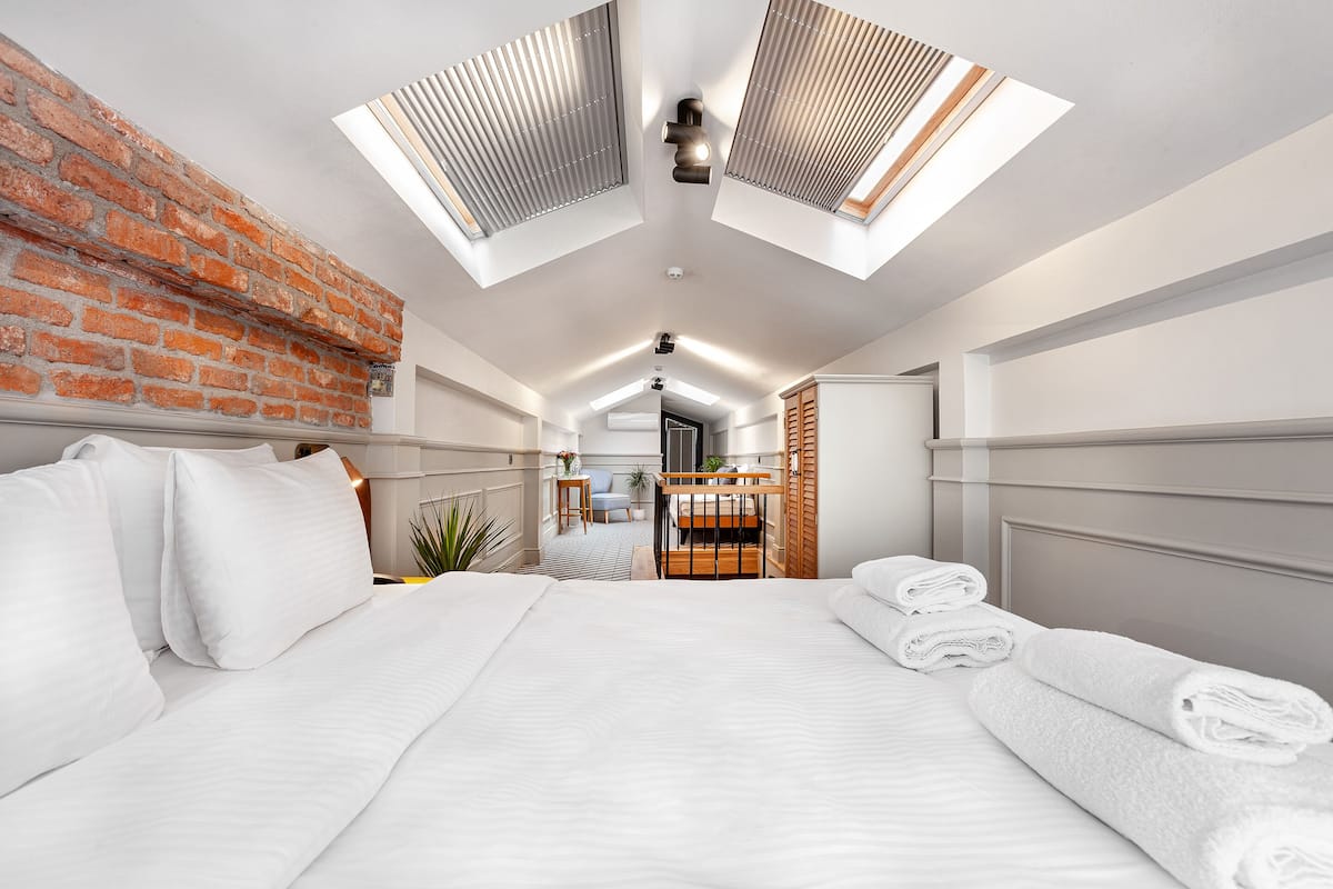 A modern hotel room with a large bed, skylights, a brick wall, and a wooden headboard.