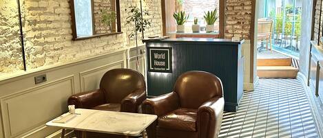 A hotel lobby with a brick wall, leather chairs, a reception desk, and a patterned floor.