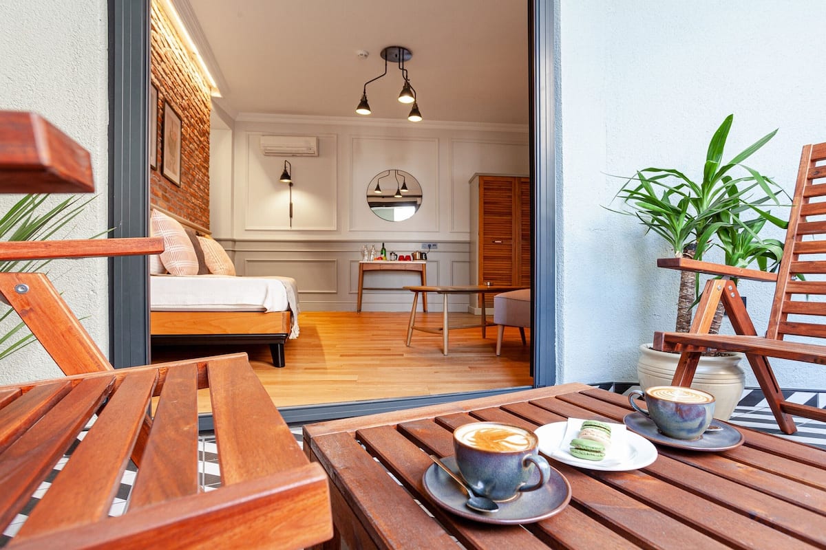 A cozy room with a bed, a wooden table with a cup of coffee and pastries, and a view of a kitchen area.