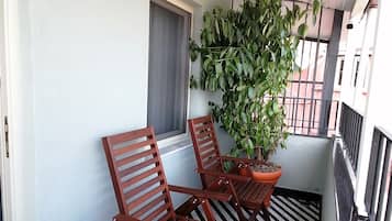 Varanda com duas cadeiras de madeira, um vaso de planta e chão com piso quadriculado em preto e branco.