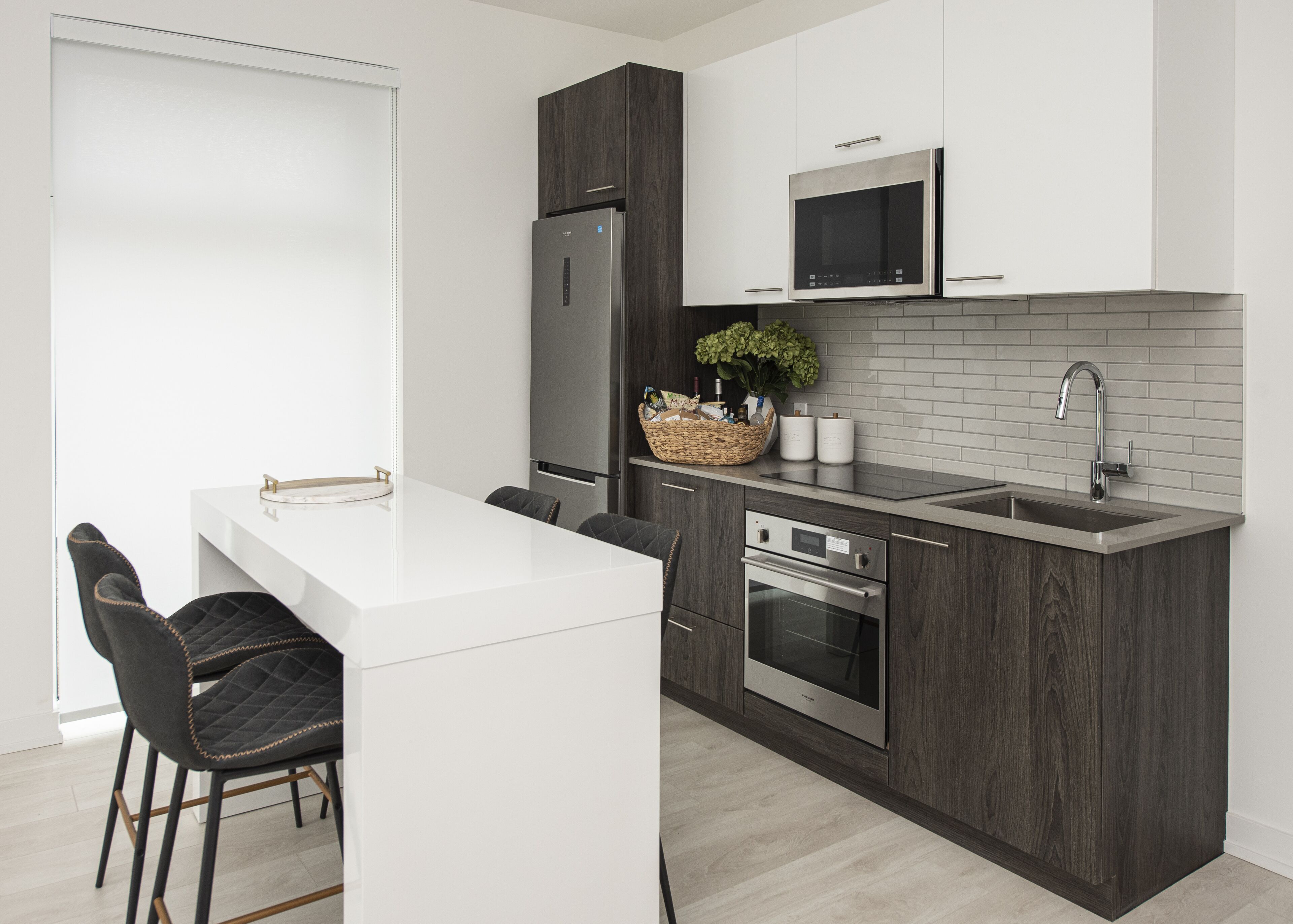 Una cocina moderna con encimera blanca, armarios de madera oscura y electrodomésticos de acero inoxidable, incluyendo un microondas integrado.