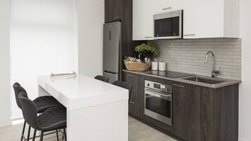 Una cocina moderna con encimera blanca, armarios de madera oscura y electrodomésticos de acero inoxidable, incluyendo un microondas integrado.