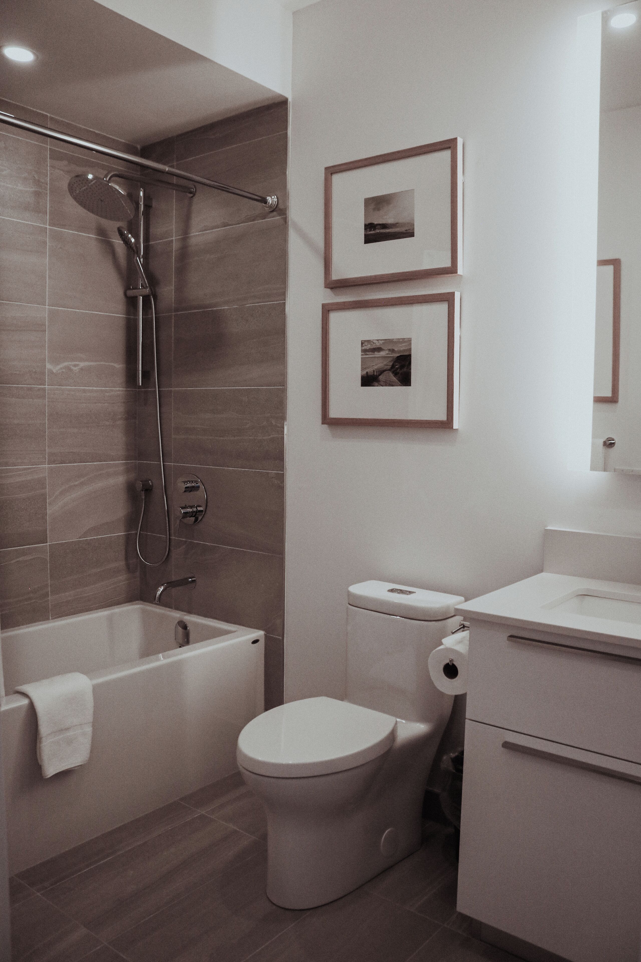 A modern bathroom with a bathtub, toilet, and shower. There are two framed pictures on the wall.