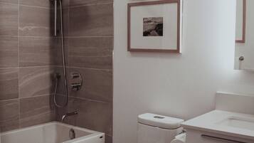 A modern bathroom with a bathtub, toilet, and shower. There are two framed pictures on the wall.