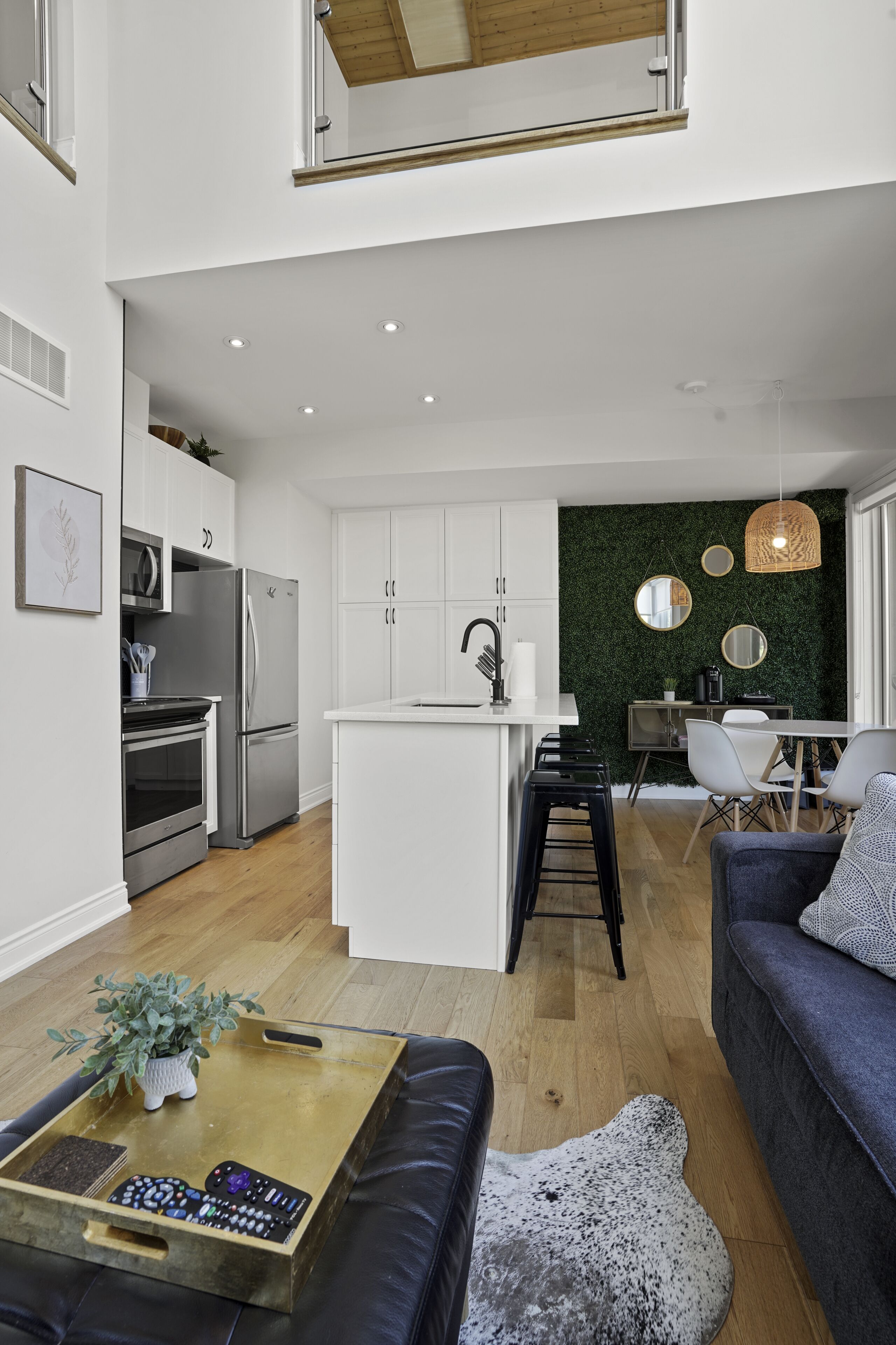 A modern kitchen with white cabinets, a central island, and a dining area with a green wall and mirrors.