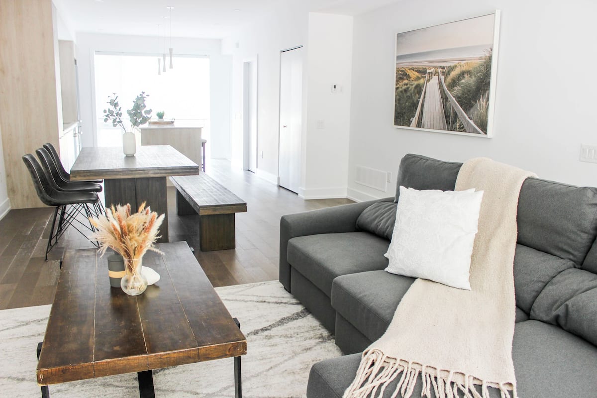 Una sala de estar moderna con un sofá gris, una mesa de centro de madera, y un comedor con sillas y una mesa.