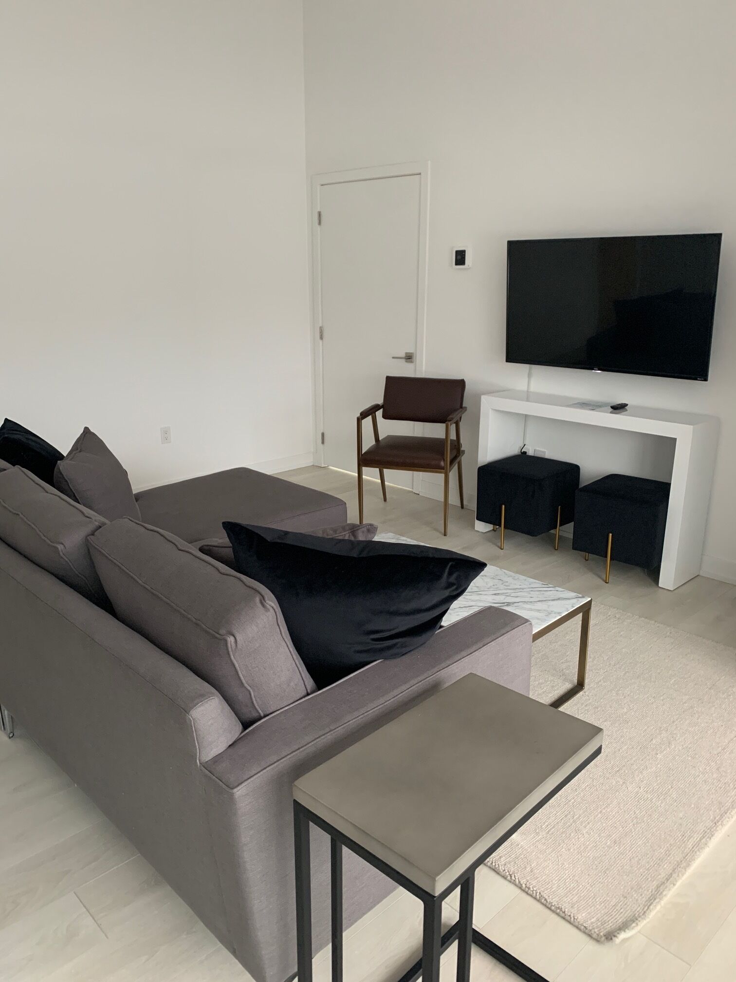 A modern living room with a grey sofa, black cushions, a small coffee table, and a flat-screen TV mounted on a white wall.