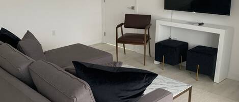 Ein modernes Wohnzimmer mit grauem Sofa, schwarzen Kissen, einem kleinen Couchtisch und einem flachbildfernseher, der an einer weißen Wand befestigt ist.