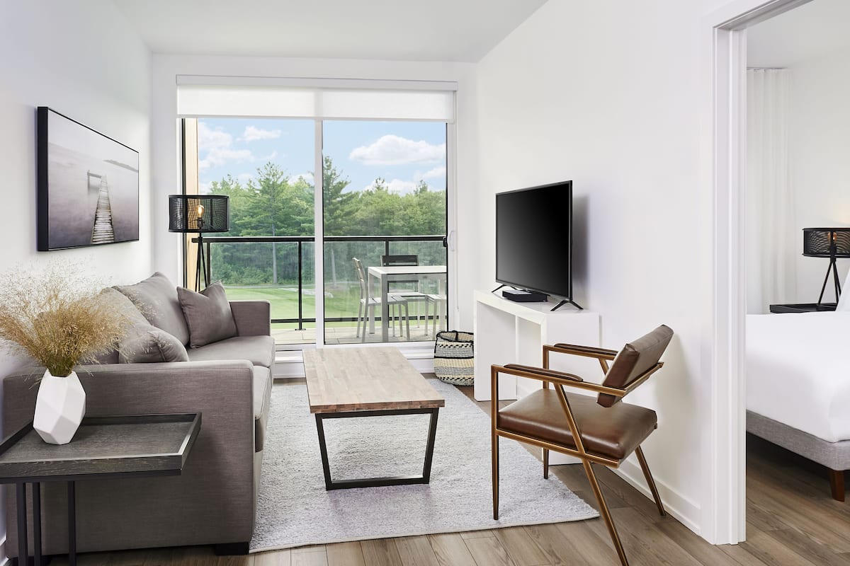 Una habitación de hotel moderna con balcón, televisor de pantalla plana, sofá, mesa de centro y cama.