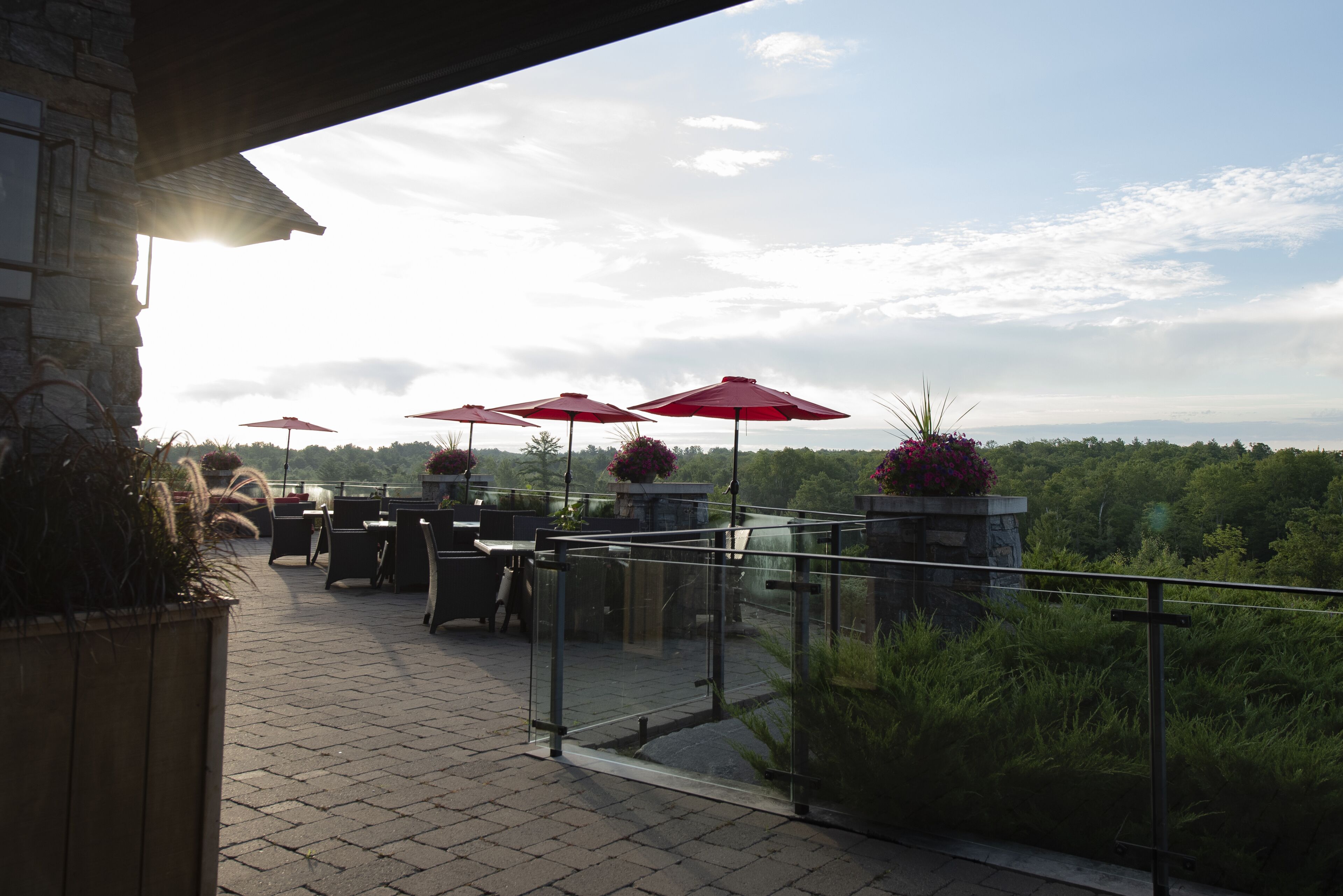 Eine Terrasse im Freien mit roten Sonnenschirmen, Steinmauern und Topfpflanzen.