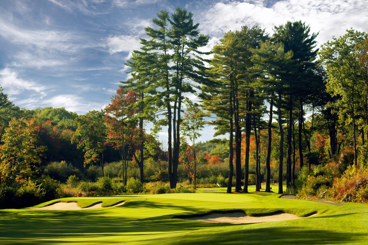 Un parcours de golf doté d’un gazon bien entretenu, de bunkers de sable, de grands arbres et d’un ciel dégagé.