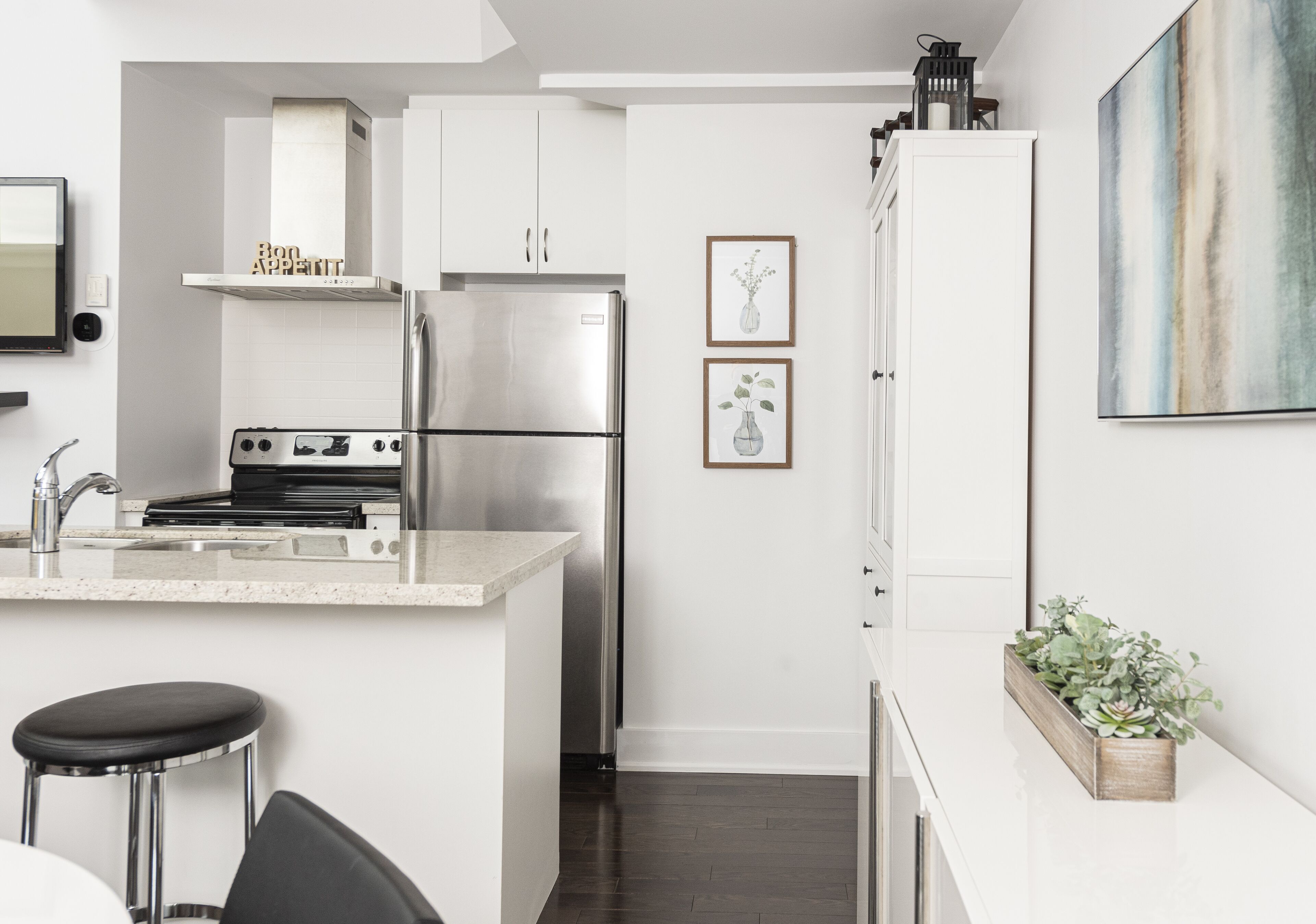 Een moderne keuken met witte kasten, roestvrijstalen apparatuur en een klein barretje met krukken.