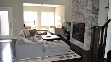 Una sala de estar moderna con chimenea de piedra, un sofá modular gris y un televisor de pantalla plana.