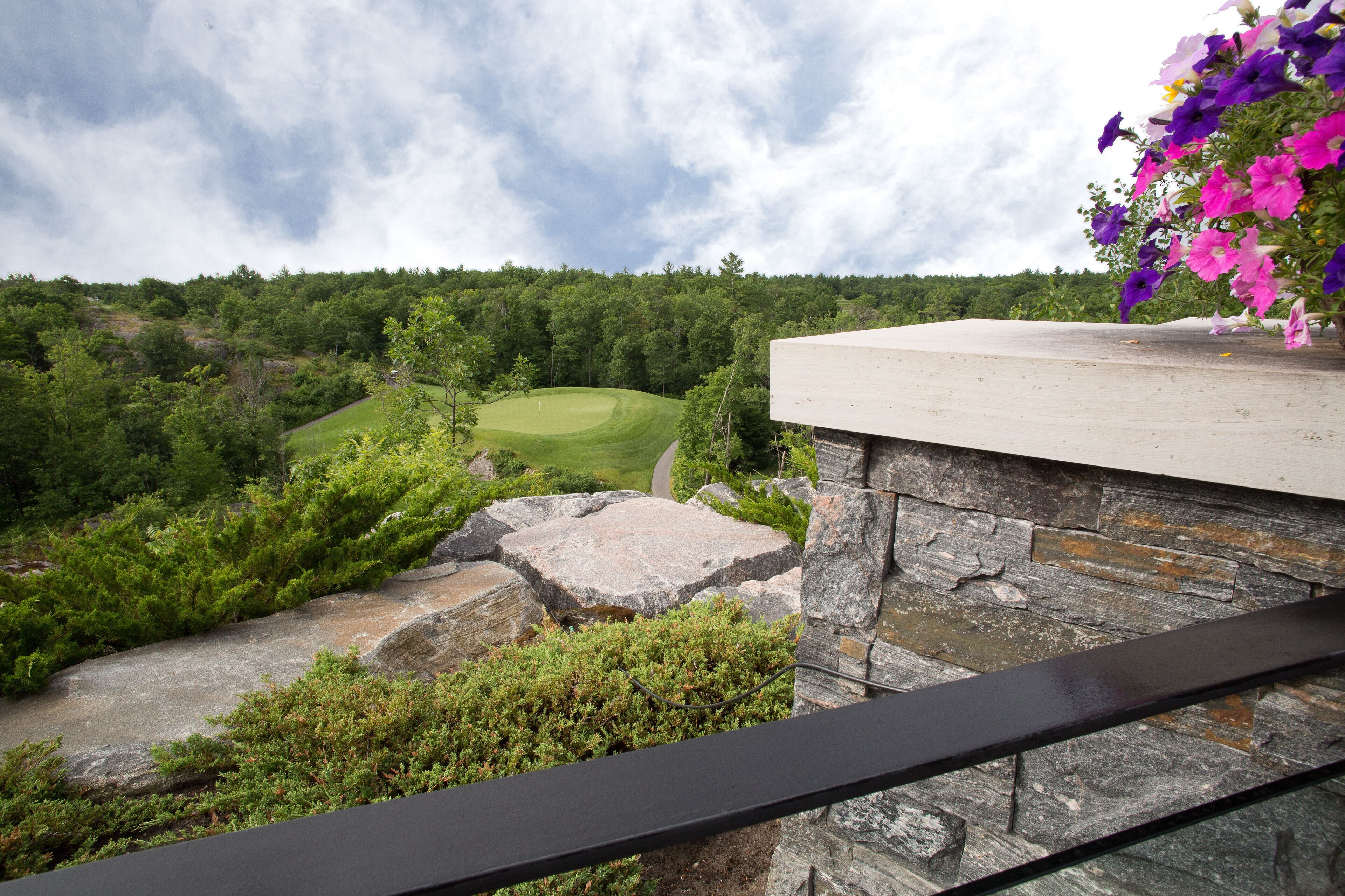Vista desde un balcón sobre un campo de golf con un muro de piedra y un arreglo floral.