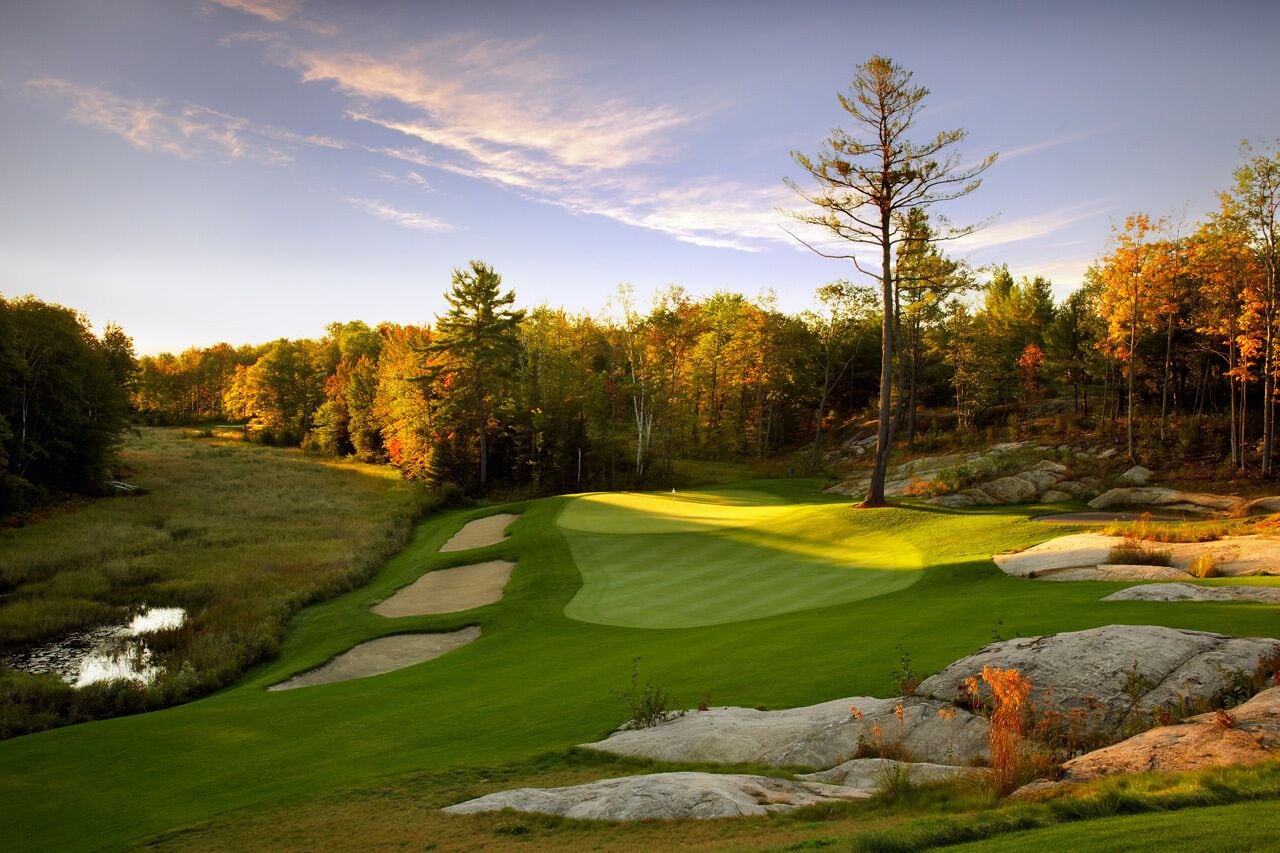 A golf course with a pond, sand bunkers, and autumn trees.
