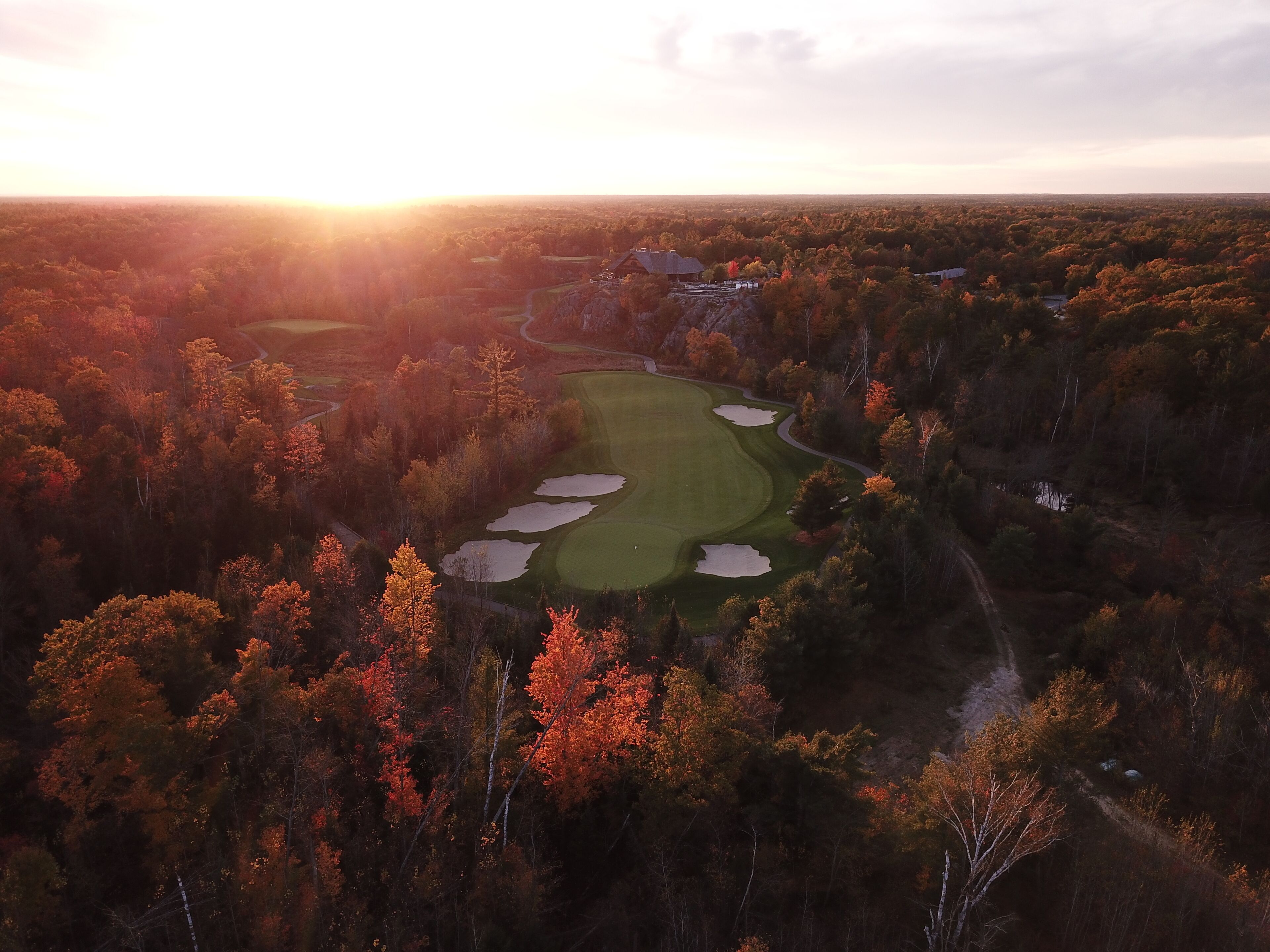 An aerial view of a golf course surrounded by autumn foliage.