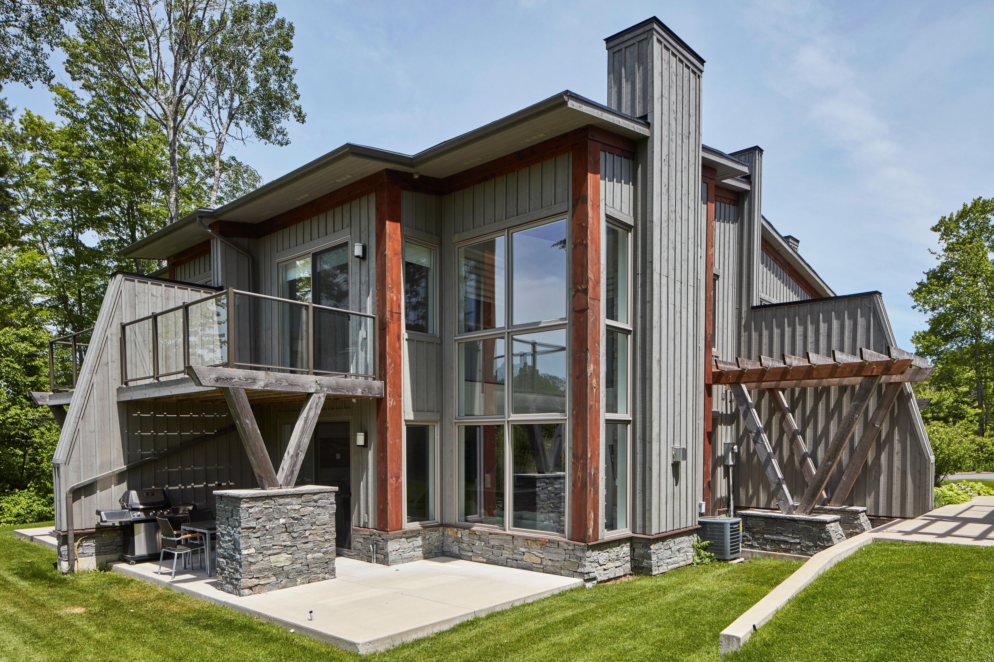 A modern house with a large glass window, a stone foundation, and a wooden deck.