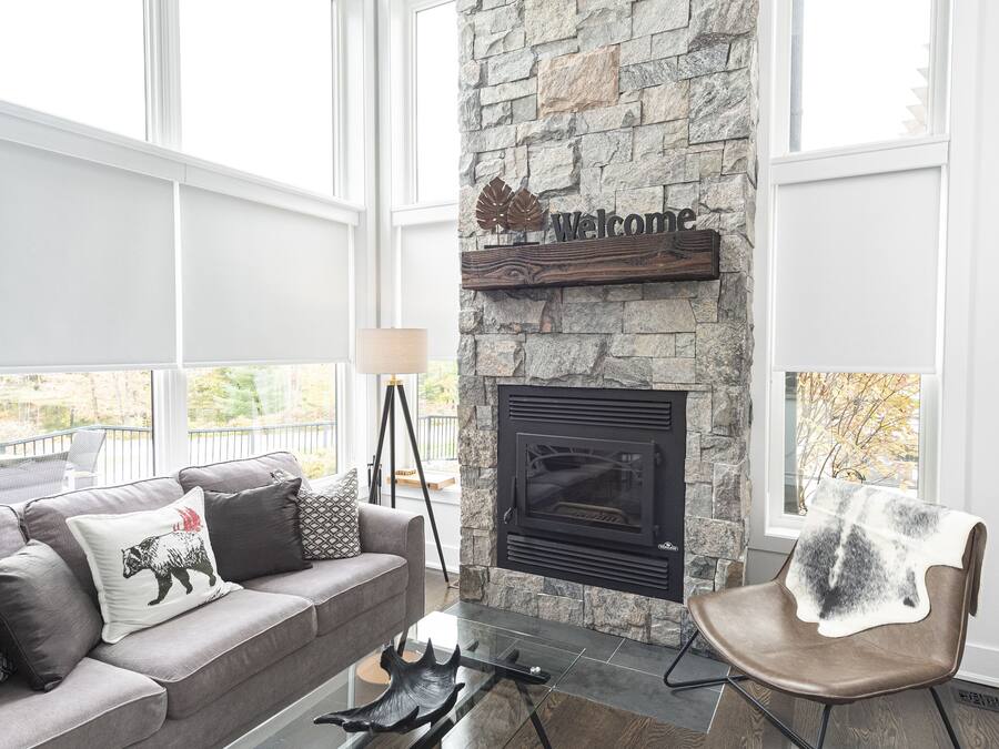 Una sala de estar moderna con chimenea de piedra, una mesa de centro de cristal, un sillón de cuero y un sofá gris con almohadones decorativos.