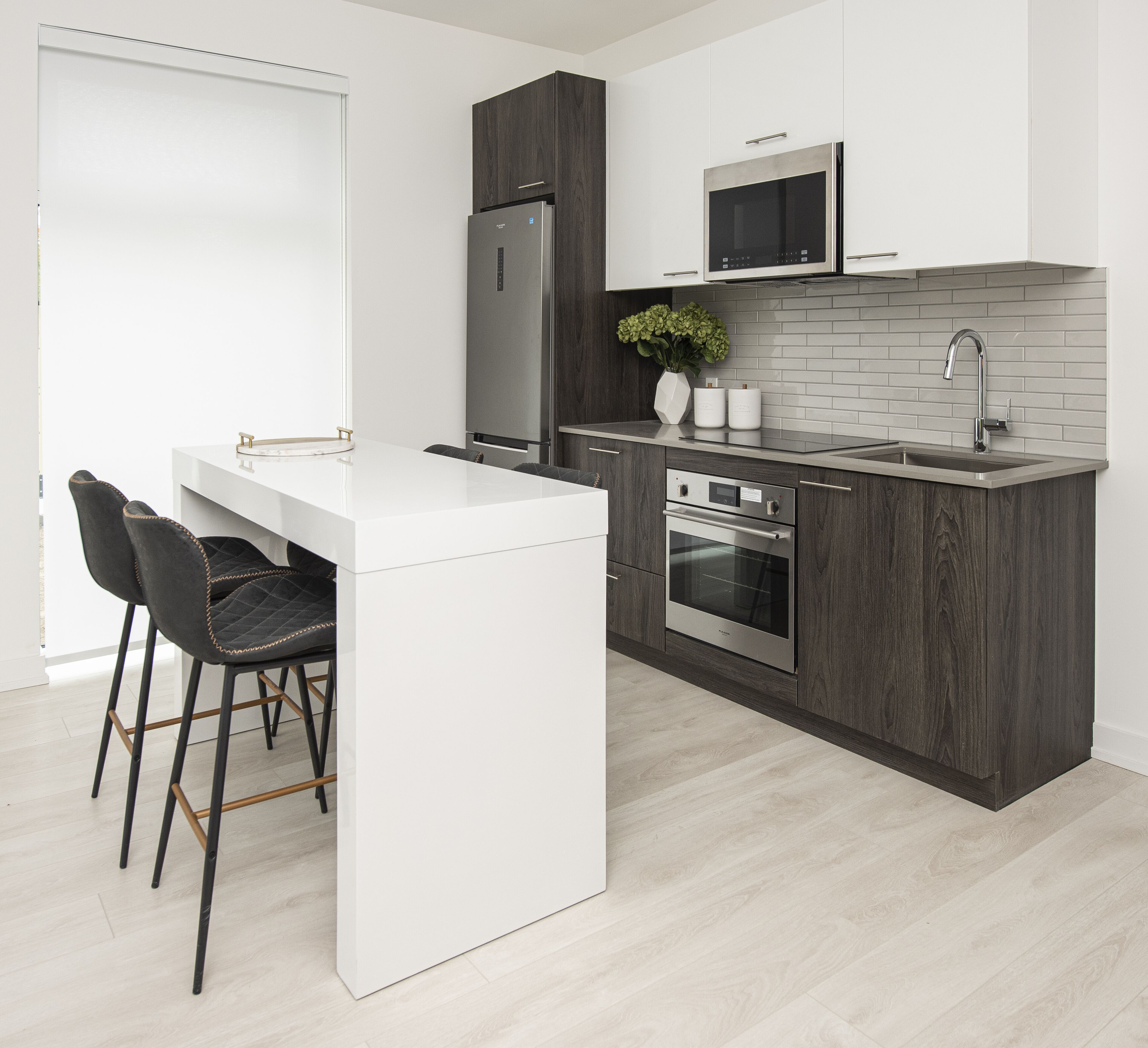 A modern kitchen with a white island, dark wood cabinets, stainless steel appliances, and a grey tiled backsplash.
