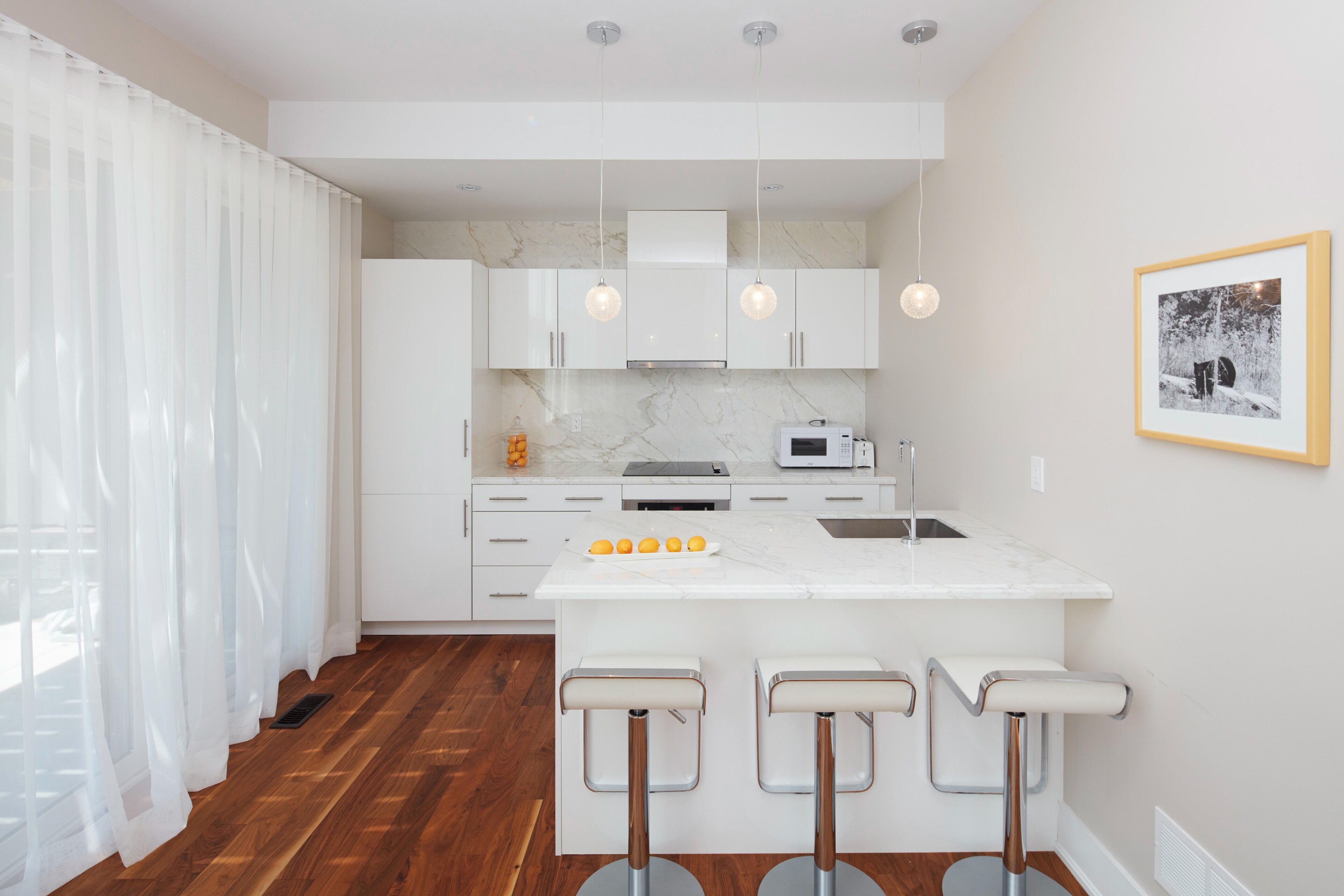 A modern kitchen with white cabinets, a marble countertop, and a central island with bar stools.