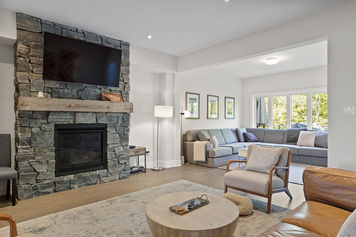 Una sala de estar moderna con chimenea de piedra, un televisor de pantalla plana grande, un sofá gris y un sofá de cuero marrón.