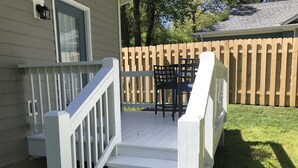 Eine Holzterrasse mit weißer Reling, eine Treppe, die zu einer überdachten Veranda führt, und ein Holzzaun im Hintergrund.