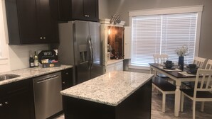 Eine moderne Küche mit dunklen Schränken, einem Edelstahl-Kühlschrank, Granit-Arbeitsplatten und einem Essbereich mit Tisch und Stühlen.