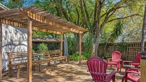 Una terraza de madera con un pérgola, un banco y sillas rojas.