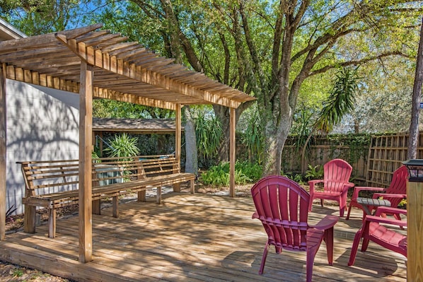 A wooden deck with a pergola, a bench, and red chairs.