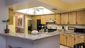 Una cocina con armarios de madera, encimeras de granito, un refrigerador de acero inoxidable, una estufa y un microondas.