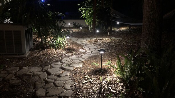 Un sendero de piedra que atraviesa un jardín con pequeñas luces distribuidas regularmente.