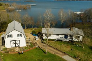 A large white building with a barn-like structure and a smaller attached building, surrounded by a well-maintained lawn and trees, with a lake in the background. - Relaxing Suite Steps to Table Rock, Near Big Cedar, Community Hot Tub & Free Daily Tickets (Hollister)
