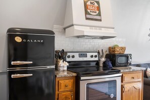 A kitchen with a black Galanz refrigerator, a Whirlpool stove, and a vintage television.