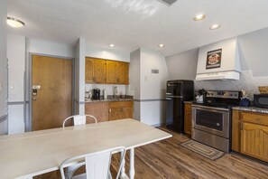 A compact kitchen with wooden cabinets, a stainless steel refrigerator, a double oven, and a dining area with a table and chairs. - Relaxing Suite Steps to Table Rock, Near Big Cedar, Community Hot Tub & Free Daily Tickets (Hollister)