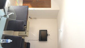 A room with a large window, a flat-screen TV mounted on the wall, and a chair with a water bottle on the table.