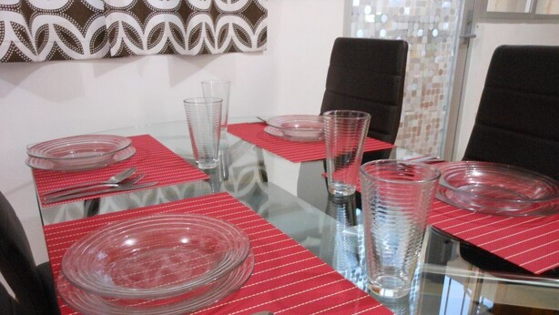 A dining table set with clear glassware and plates, red striped placemats, and black chairs.