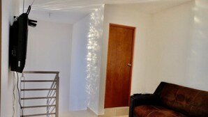 A living room with a sofa, a television mounted on the wall, a wooden door, and a staircase.