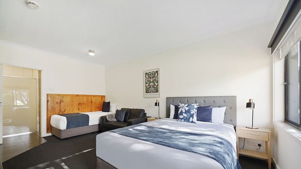 A modern hotel room with a large bed, a sofa, a bedside table, and a window. - Hamilton Lakeside Motel (Hamilton)