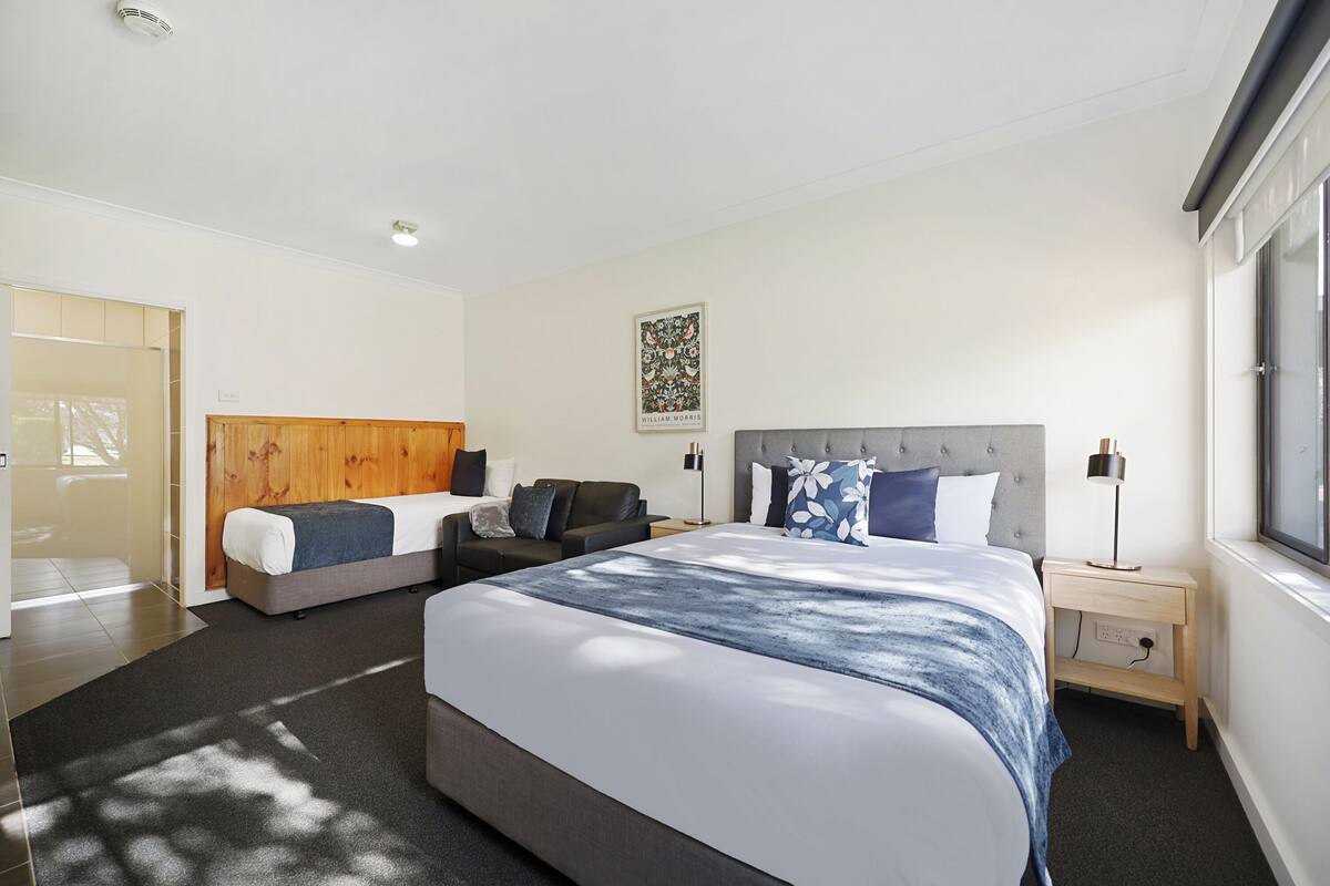 Quarto de hotel moderno com uma cama grande, um sofá, uma mesinha de cabeceira e uma janela.