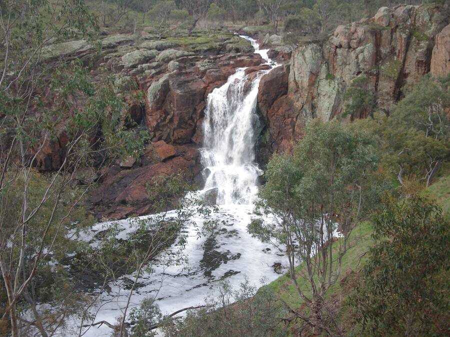 A waterfall cascading down a rocky cliff surrounded by dense vegetation.