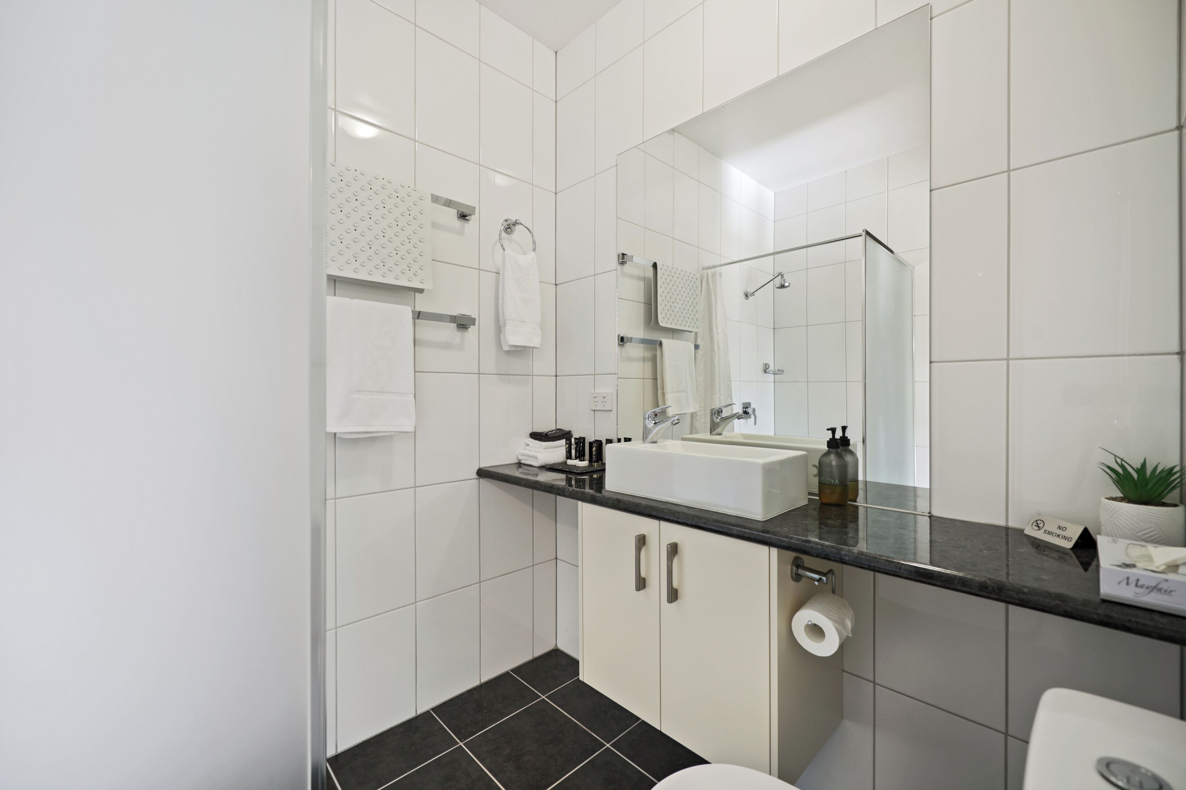 A modern bathroom with a large mirror, white tiles, a black countertop, and a toilet.