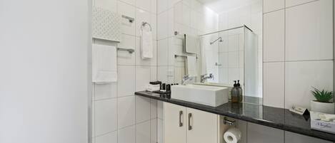 A modern bathroom with a large mirror, white tiles, a black countertop, and a toilet.