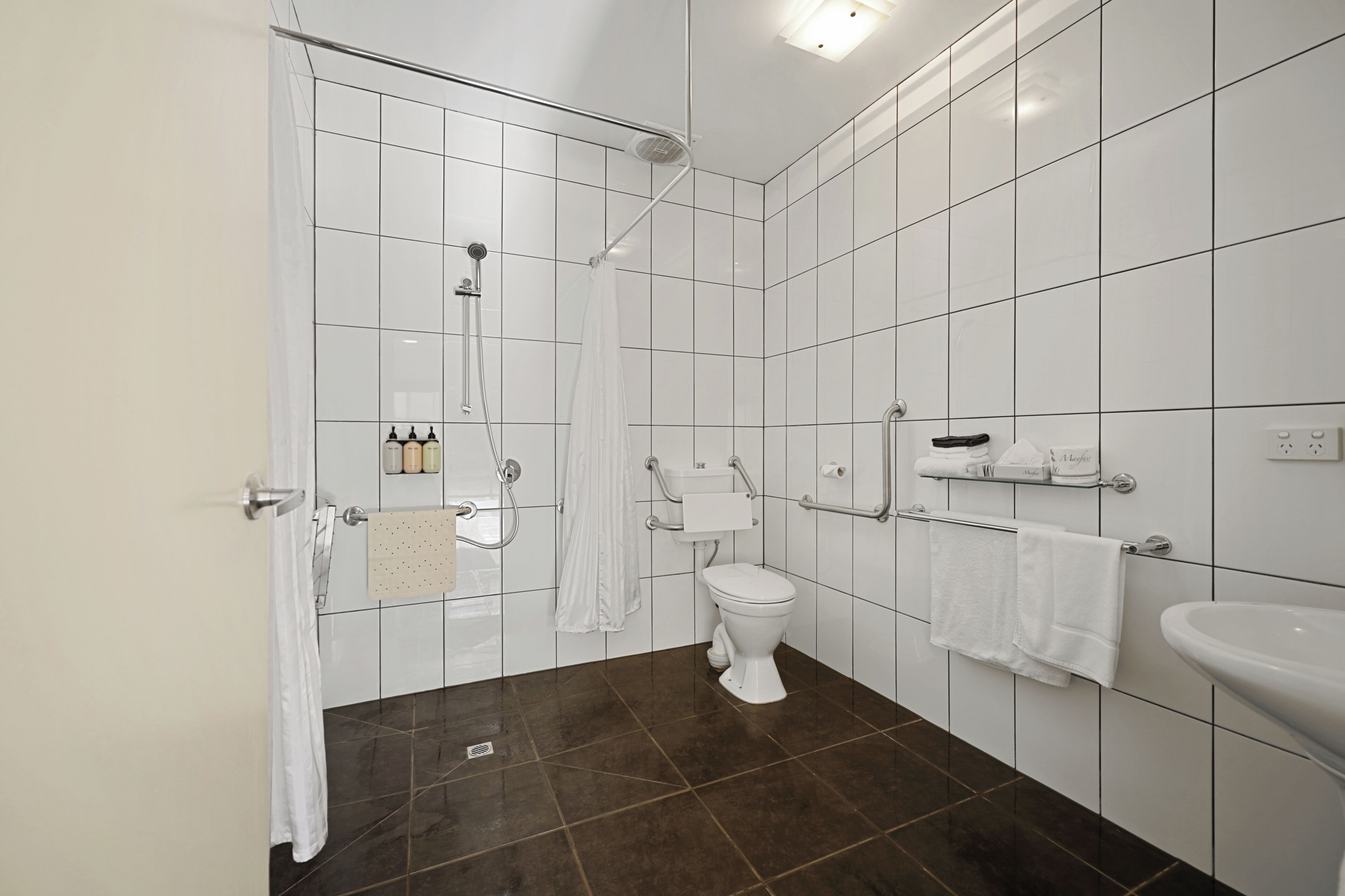 Een moderne badkamer met witte tegels, een douche, toilet en wastafel.