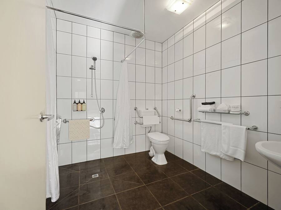 Een moderne badkamer met witte tegels, een douche, toilet en wastafel.