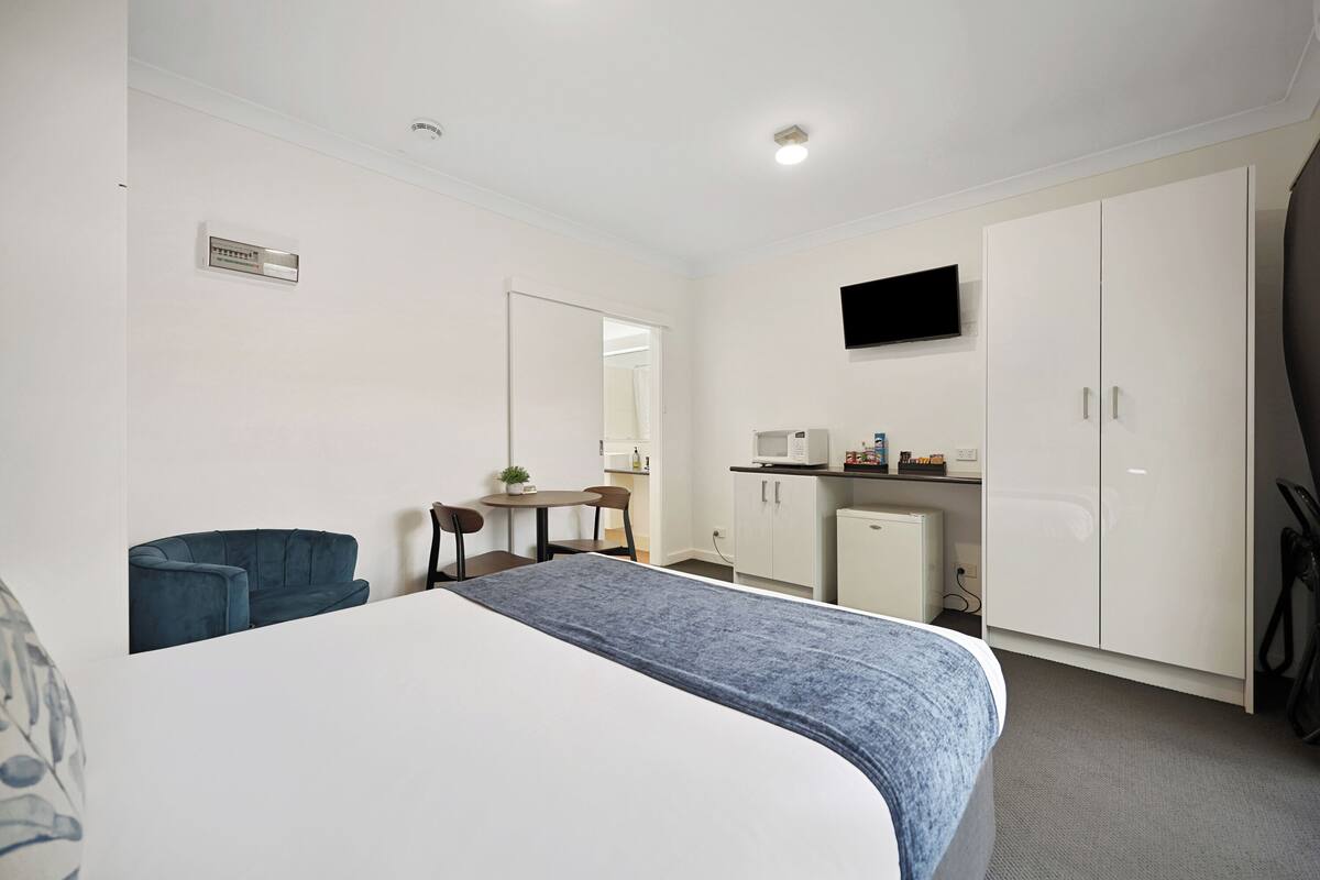 Quarto de hotel com uma cama, uma escrivaninha, uma cadeira, televisão e guarda-roupa.